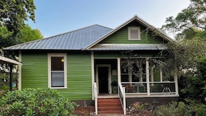 A green house with a front porch, a small entryway, and a garden area with various plants and a stone pathway. - Historic 3-bedroom home in beautiful Athens. Walkable to town and Campus. (Athens)