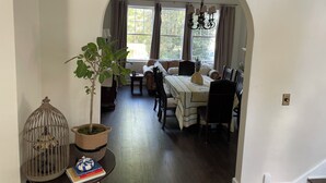 Uma sala de jantar com mesa posta para quatro pessoas, um candelabro e vista pela janela com cortinas.