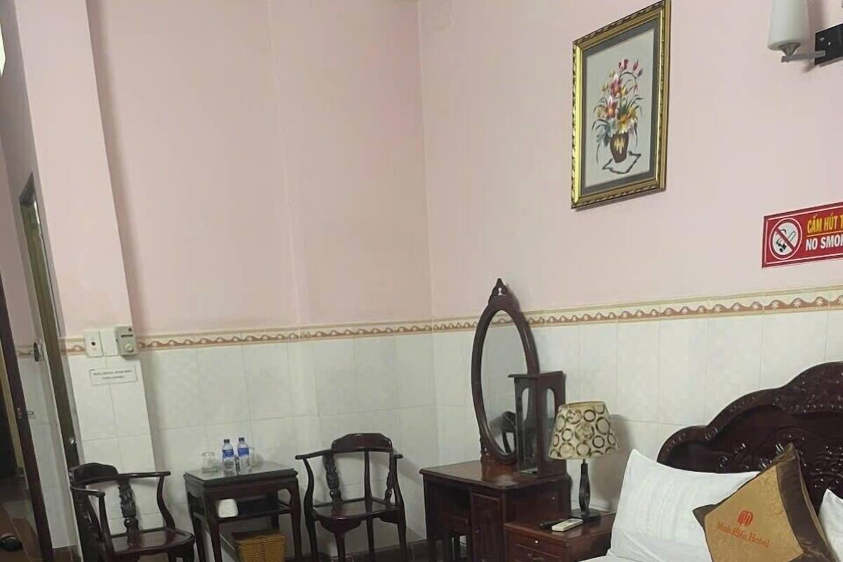 Une chambre d’hôtel comprenant un lit, un bureau, deux chaises, un miroir et un panneau fixé au mur.