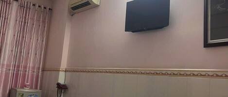 A hotel room with a bed, an air conditioning unit, a flat-screen TV, and a wall-mounted phone.