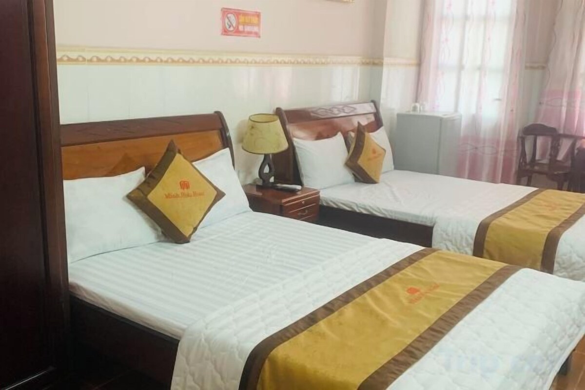 A hotel room with two beds, each with a wooden headboard, a nightstand, a lamp, and a chair.