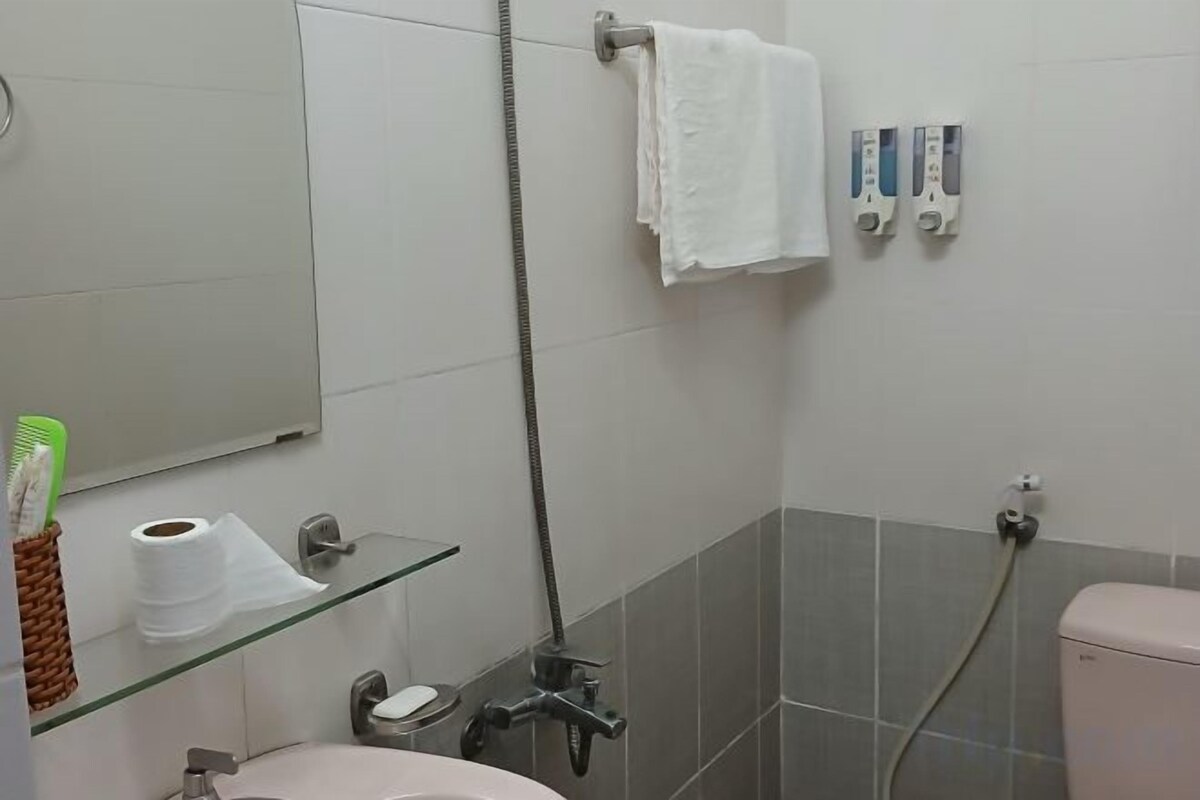 Une salle de bain avec une étagère en verre où sont rangés les articles de toilette, des toilettes et une douche avec un flexible.
