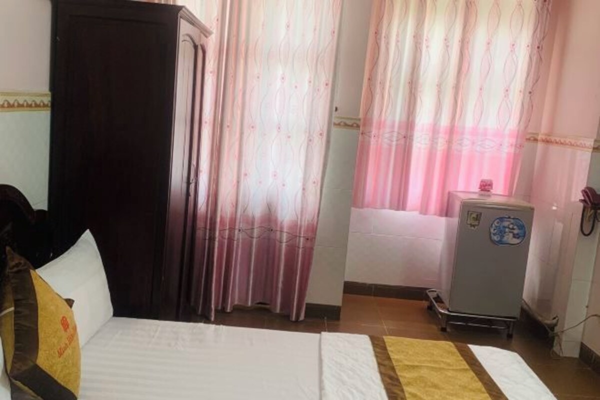 Een hotelkamer met een bed, gordijnen, een kledingkast en een kleine koelkast.