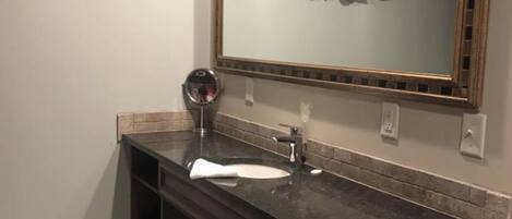 A bathroom with a dark countertop, a sink, a mirror, and a towel rack.