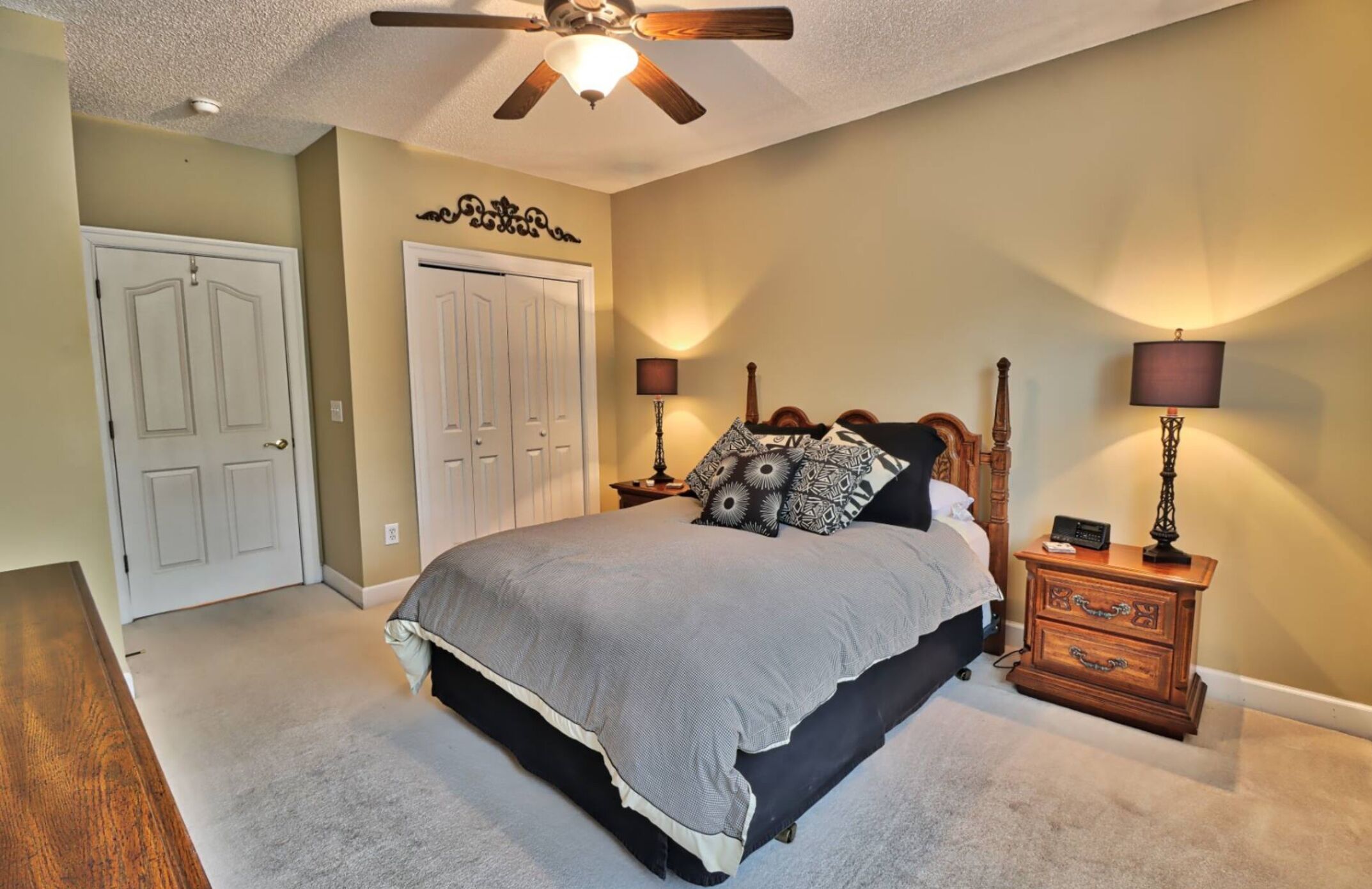 A bedroom with a bed, two bedside tables, a ceiling fan, and a door.