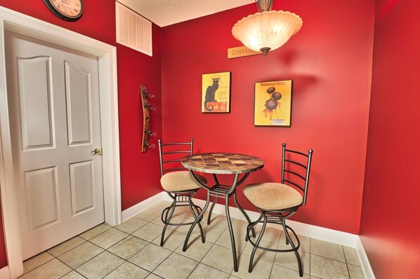 A dining area with a red wall, a white door, a round table with four chairs, and two wall-mounted posters. - Beautiful Barefoot Golf Resort Condo (North Myrtle Beach)