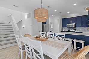 A modern kitchen with dark blue cabinets, a white dining table with chairs, and a hanging light fixture. - Golf Cart/Bikes/DogsOK/Walk2Beach (Santa Rosa Beach)