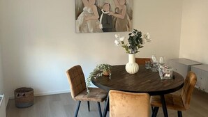 A dining area with a round table, four chairs, a vase with flowers, and a painting on the wall. - Holidayhome De Molen (Noordwijk)