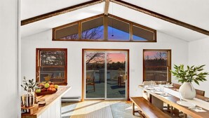 A dining area with a wooden table and benches, large windows, and a view of the backyard. - Lakefront Summer Getaway w/ HotTub+Games+FirePit (Long Pond)