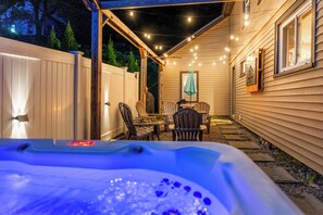 A hot tub in a covered outdoor area with a wooden deck, chairs, and string lights.