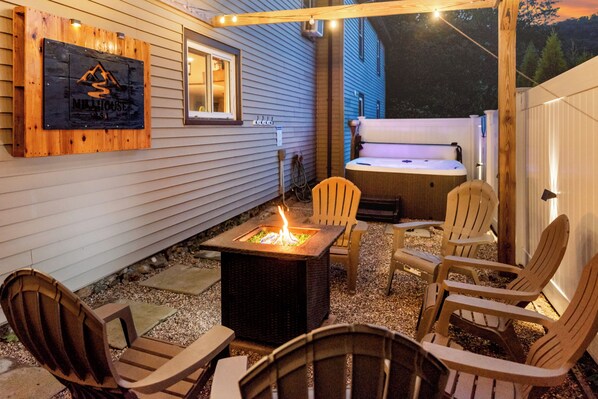 An outdoor patio area with a fire pit, seating, and a hot tub.