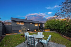 A modern house with a dark exterior, a visible garage, and a small patio with a table and chairs. - Luxury Spa, Patio, Deck & Views of Puget Sound in the Heart of Old Town, Tacoma (Tacoma)