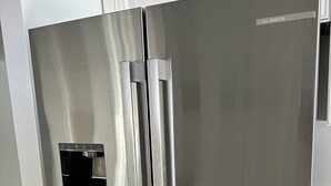 Frigorifero in acciaio inossidabile dotato di erogatore d'acqua, posizionato in una cucina con mobili bianchi.