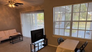 A living room with a sofa, a TV, a table, and a window with blinds. - Cozy 1-bedroom with AC, WiFi in charming Plant City (Plant City)
