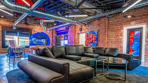 A modern lounge with a sectional sofa, a glass coffee table, and a brick wall with exposed ductwork. - b3 Room4: Begin King Suite (Sparta)