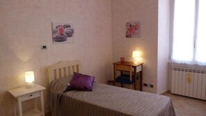 A bedroom with a bed, bedside tables, a nightstand, a chair, and a window.