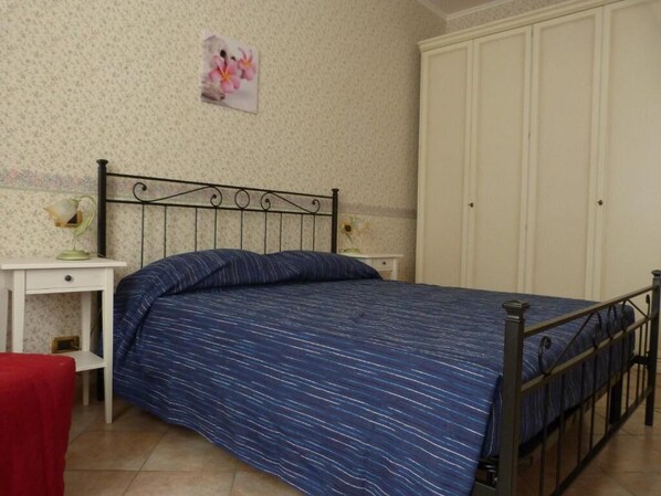 A bedroom with a bed, a nightstand, a wardrobe, and a wall with a floral picture.