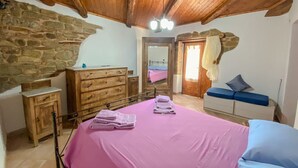 A bedroom with a bed, wooden dresser, and a stone wall.