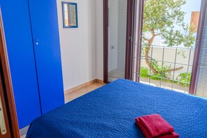 Relax in this serene bedroom with a large bed, a balcony offering a tree-lined view, and a convenient wardrobe with a mirror.
