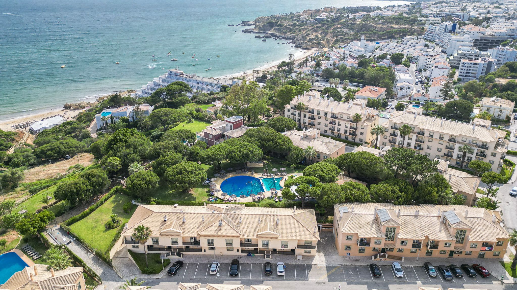 A coastal residential area with a swimming pool surrounded by greenery, adjacent to a beach.