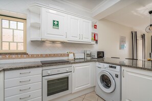 A modern kitchen with white cabinetry, a built-in oven, a microwave, and a washing machine.