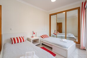 A hotel room with two single beds, a large mirror, a wardrobe, and a red and white striped pillow.