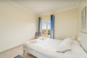 Una habitación de hotel con una cama, una silla, un balcón con cortinas y vistas a edificios.