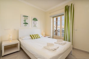 Una habitación de hotel con cama, mesita de noche, ventana con cortinas y una obra de arte en la pared.