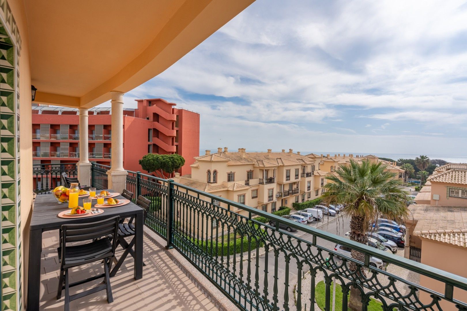 Un balcone con un tavolo apparecchiato per la colazione, con vista su una zona residenziale caratterizzata da edifici e un cielo sereno.