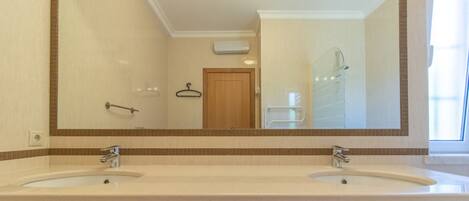 A bathroom with two sinks, a large mirror, and a shower.