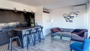 A modern kitchen with a bar area, a grey sofa, and a blue armchair. - Chic Sea View Apartment by Hello Homes Sitges (Sitges)
