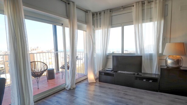 A modern living room with a large window, a flat-screen TV, a lamp, and a chair. - Chic Sea View Apartment by Hello Homes Sitges (Sitges)