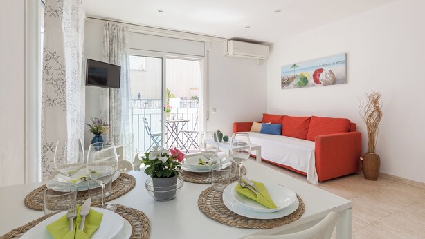 Een eethoek met een witte tafel gedekt voor vier personen, een rode bank en een balkon met uitzicht.