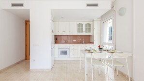 Een moderne keuken met witte kasten, een eethoek met een witte tafel en stoelen, en een raam met uitzicht.