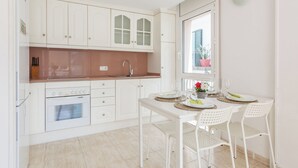 Een moderne keuken met witte kastjes, een inbouwoven en een eethoek met een tafel en stoelen.