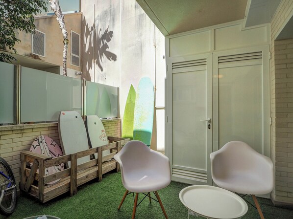 A patio area with surfboards, a bicycle, and two white chairs. - La Perla by Hello Homes Sitges (Sitges)