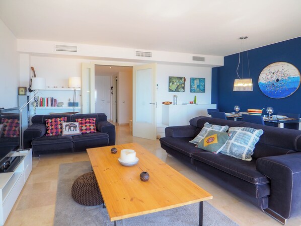 Un salon moderne avec deux canapés, une table basse en bois et un coin repas avec une table dressée pour deux personnes.