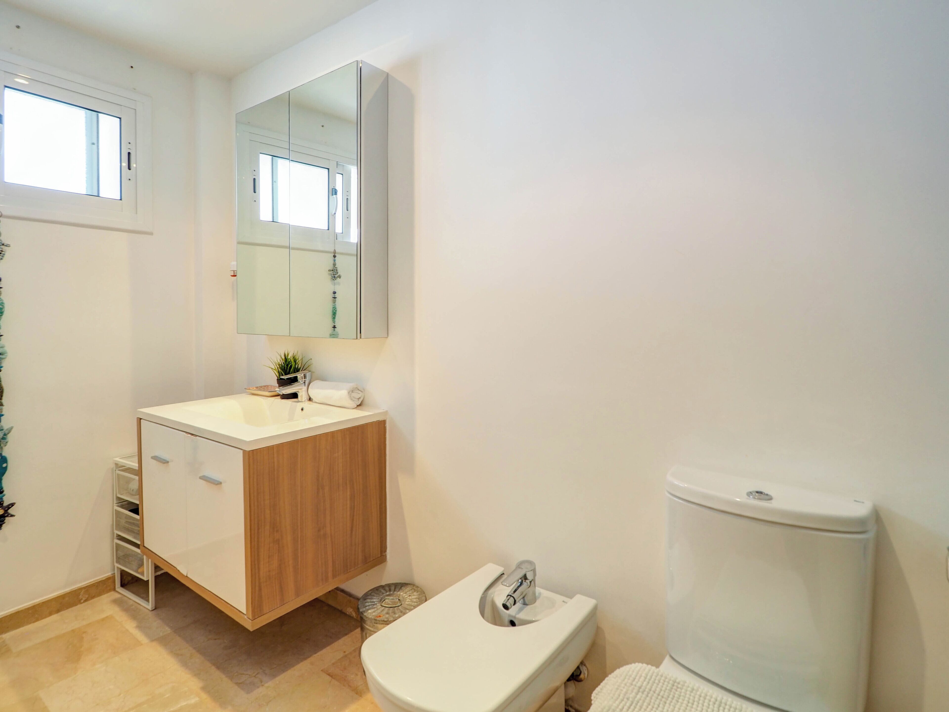 Un baño moderno con un lavamanos blanco, tocador de madera, un espejo sobre el lavamanos y un inodoro blanco.