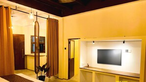 A hotel room with a bed, a TV mounted on the wall, a small desk, and a potted plant.
