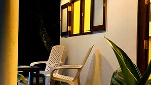 An outdoor seating area with a white plastic chair, a wooden table, and a potted plant.