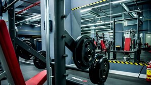 Un gimnasio con equipo de levantamiento de pesas, espejos y una banca roja.
