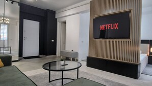 Una sala de estar moderna con un televisor de pantalla plana grande montado en un panel de madera, una mesa de centro redonda de vidrio, un sofá y un escritorio con una silla.