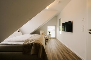 A modern bedroom with a sloped ceiling, a bed, a TV, and a small side table with a plant. - De Diek - Suite 4 | Lateral dike location (Greetsiel)