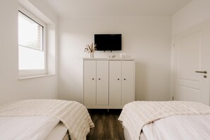 A bedroom with two beds, a TV on the wall, a cabinet, and a window.