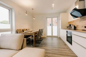 A modern kitchen with a dining area, wooden flooring, and a large window.