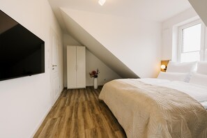 Une chambre avec un plafond en pente, un lit, un téléviseur fixé au mur et une fenêtre.
