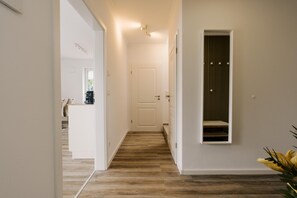 A hallway with a wooden floor, white walls, and a door at the end.
