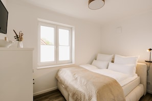 A bedroom with a bed, a window, a bedside table, and a lamp.