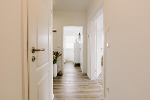 A hallway with a wooden floor, white walls, and a door on the left.
