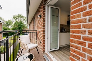 A balcony with a wicker chair and a table, a sliding glass door, and a brick wall.